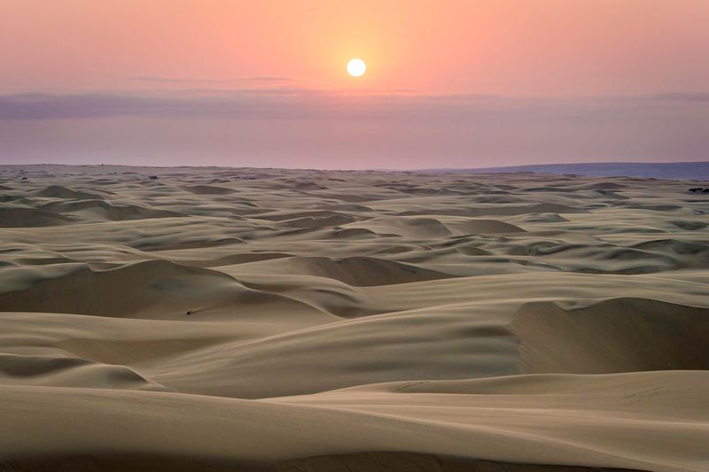 Wüstenlandschaft in der Dämmerung, dahinter die Sonne