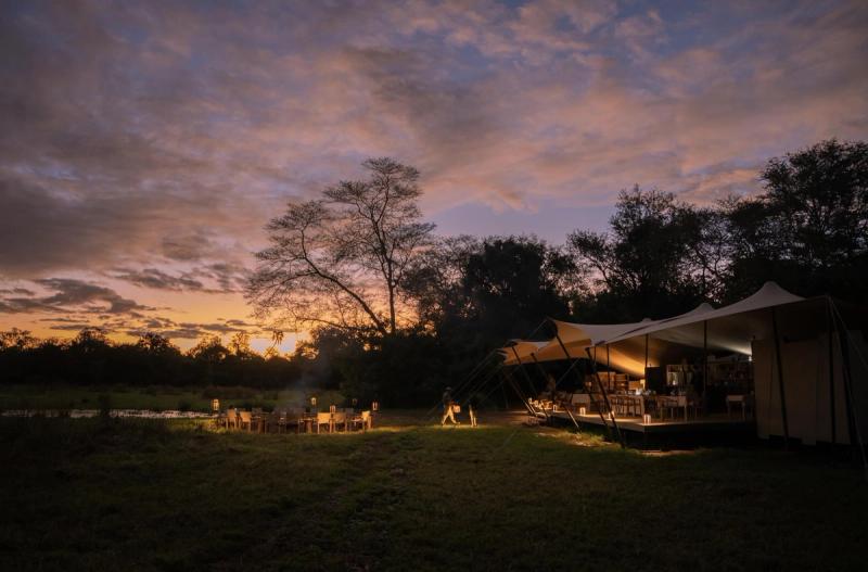 A softly lit safari camp glows beneath a dramatic sunset sky, showing how thoughtful tourism supports conservation through the impact in Gorongosa.