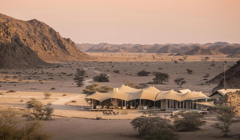 A remote desert camp sits beneath sweeping rocky ridges, capturing the stark beauty of where to go in 2026.