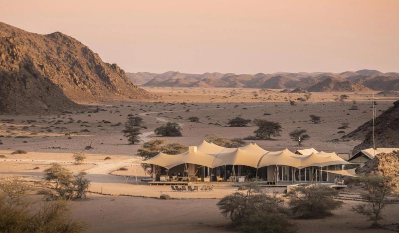 A remote desert camp sits beneath sweeping rocky ridges, capturing the stark beauty of where to go in 2026.