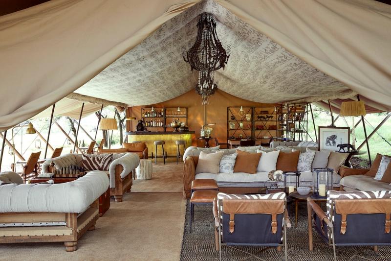 An opulent lounge area with chandeliers, plush sofas, and a brass bar shows the unexpectedly lavish interior of mobile tented camps in Tanzania.