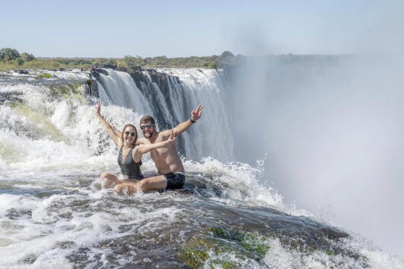 A couple poses with raised arms in Devil’s Pool, perched daringly at the edge of the best side of Victoria Falls.
