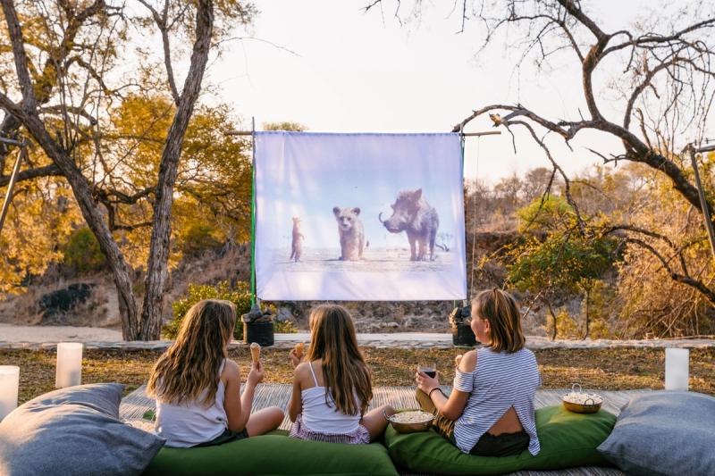 Three children watch The Lion King under the stars at a bush cinema, showing how Africa's best destinations for kids mix safari thrills with familiar comforts.