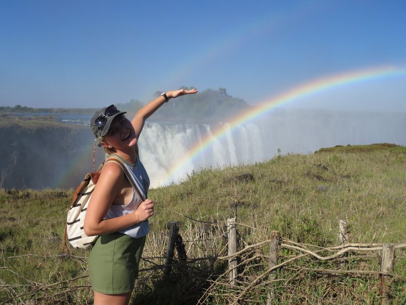 A Rhino Africa travel consultant standing in front of a rainbow with Victoria Falls in the background