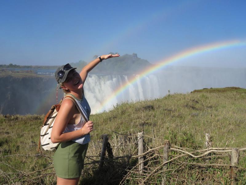 A Rhino Africa travel consultant standing in front of a rainbow with Victoria Falls in the background