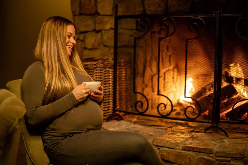Katharina lounges by a cosy fireplace, cradling a warm cup of tea and laughing during her babymoon safari.