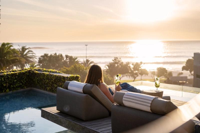 A woman lounges poolside with cocktails, overlooking the ocean from one of the luxury hotels in Cape Town