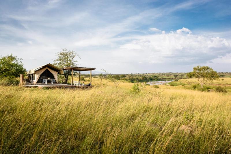 A solitary canvas tent on a raised wooden deck overlooks golden grasslands and a winding river, embodying the remote intimacy of Luxury safari lodges in Tanzania.