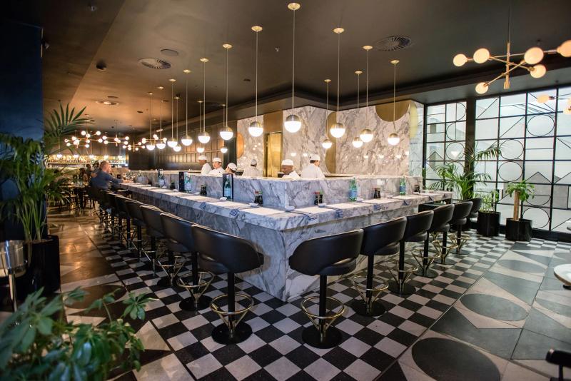 A large, white marble-clad sushi bar, black steel finishes, and checkered floor tiles