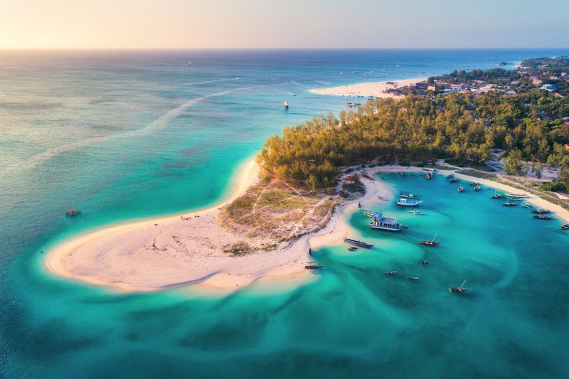 An aerial view of a white-sand peninsula surrounded by turquoise water and moored boats off the coast of Zanzibar