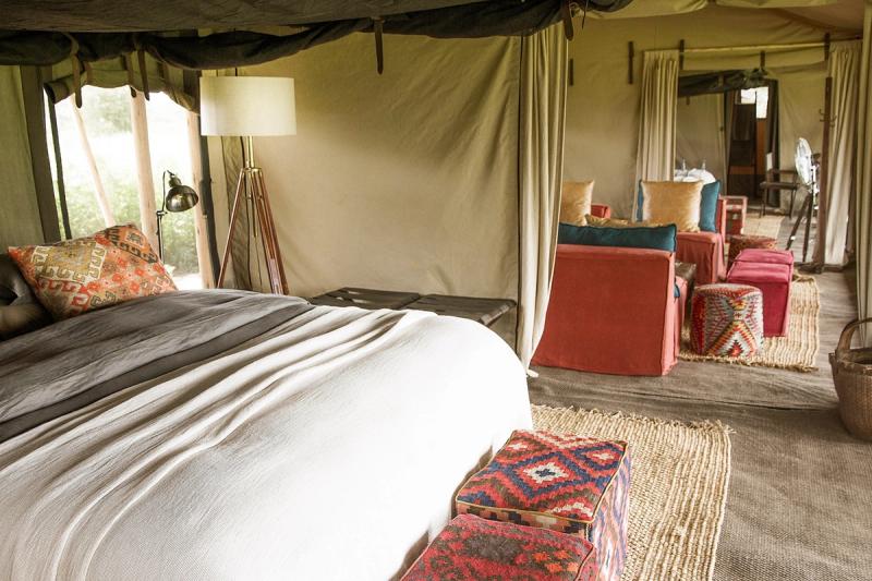 A spacious interior of one of Tanzania’s mobile tented camps features a king-sized bed, woven rugs, and colourful lounge seating beneath canvas walls.