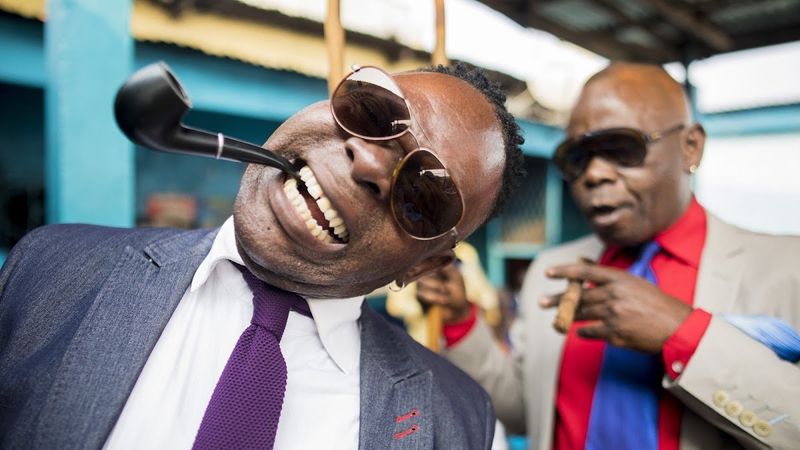 Two sapeurs in smart clothes with sunglasses and a pipe in their mouths pose for the camera
