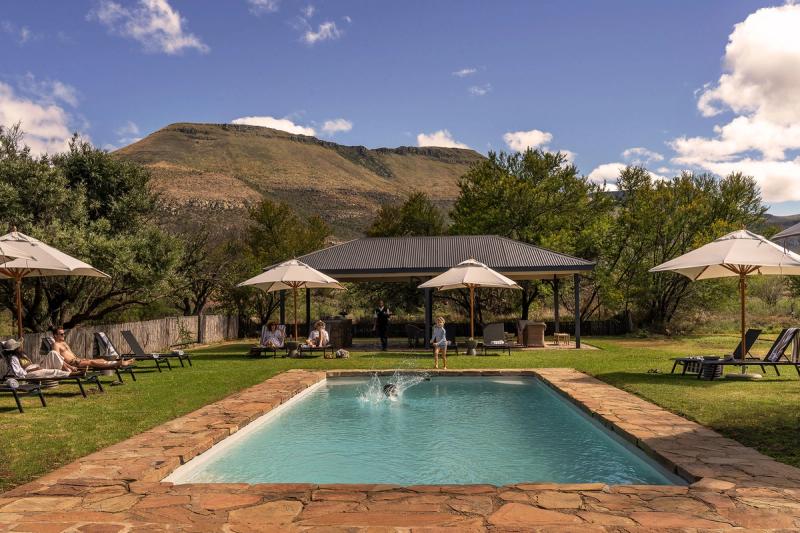 Guests relaxing around the swimming pool at Samara Karoo Lodge with mountain views.