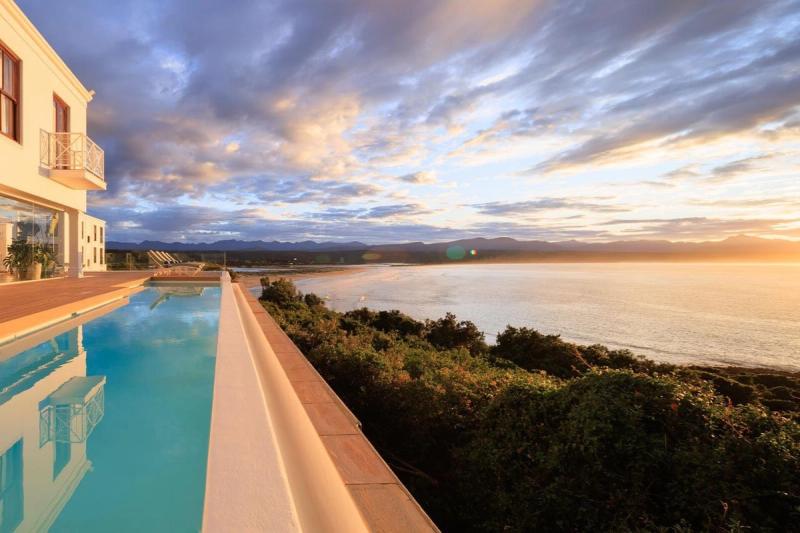 A luxurious poolside view overlooking a serene beach and rolling hills, illuminated by the soft light of a sunset sky.
