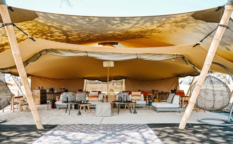 A stylish open-plan lounge at one of Africa’s mobile tented camps features relaxed seating, woven textures, and a floating canopy roof.