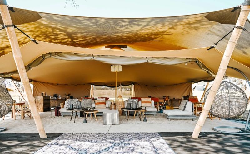 A stylish open-plan lounge at one of Africa’s mobile tented camps features relaxed seating, woven textures, and a floating canopy roof.
