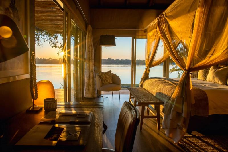 Mauritius and safari holiday, a luxurious safari lodge suite glows in the golden sunrise, with a four-poster bed draped in soft netting and a private deck overlooking the tranquil Zambezi River.