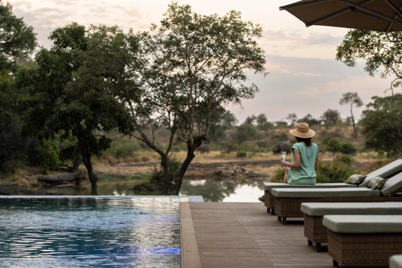 A woman enjoys a glass of sparkling wine beside the pool at Tanda Tula, overlooking the surrounding bush.