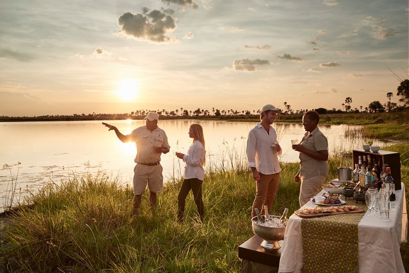 Guests sharing sundowners and conversation with local staff in Botswana 