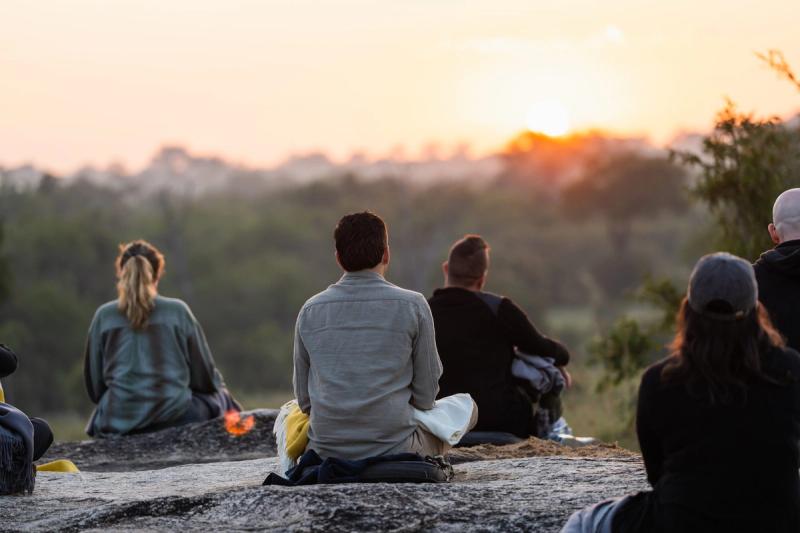 A group of people doing a sunrise meditation from the top of a large rock in the Sabi Sand Game Reserve, looking out over the bush