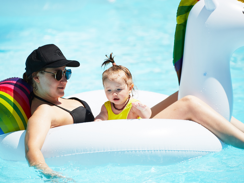 A mother lounges with her baby on a unicorn float in a pool, highlighting how the best destinations for kids can still cater to comfort-seeking parents of tiny travellers.