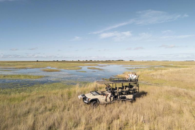 A raised safari vehicle pauses beside a wetland as guests observe the open plains, exemplifying immersive destinations for responsible travel.