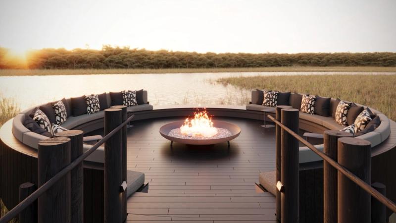 A circular outdoor fire pit with curved cushioned seating overlooks the water at sunset, setting the scene for one of the new luxury safari lodges 2026.