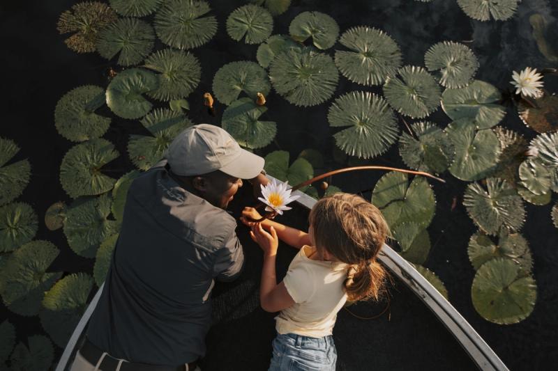 A young girl and guide examine a water lily from a boat surrounded by lily pads, illustrating how the best destinations for kids in Africa can offer immersive, hands-on nature experiences.