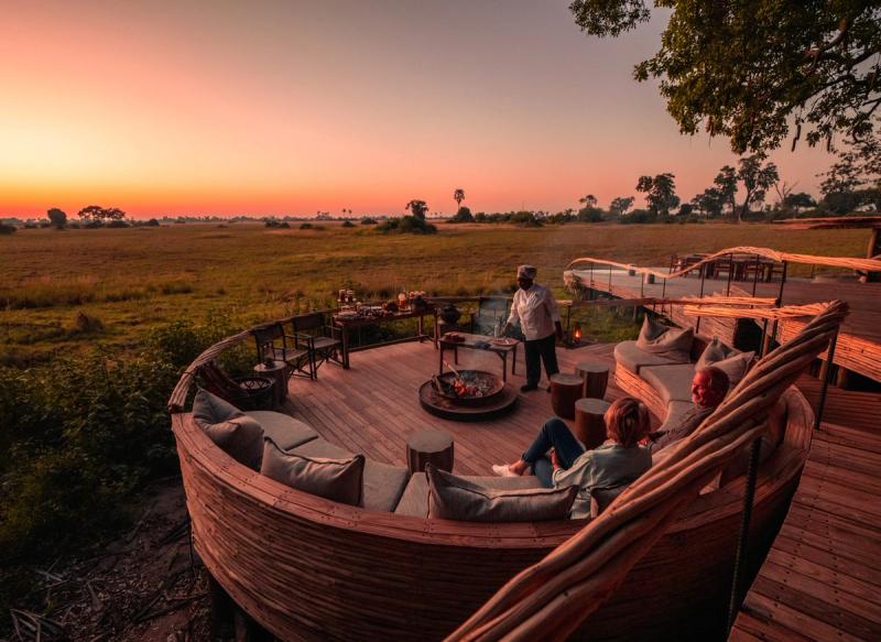 Guests relax around a firepit on a stylish deck overlooking the savannah at sunset, soaking in the magic of African travel in May.