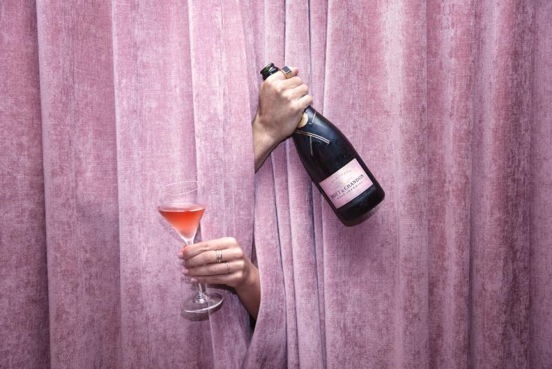 A bottle and glass of Rosé Champagne in front of a velvet drape curtain