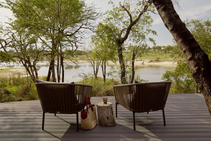 Two woven lounge chairs on a wooden deck face a quiet lake through riverine trees, capturing the unhurried intimacy that defines lodges with the best waterholes.