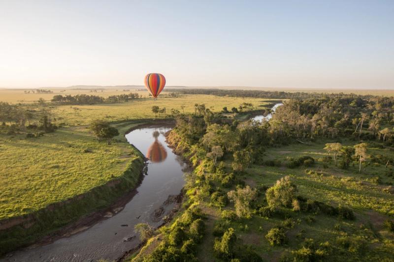 A hot air balloon safari over the Maasai Mara's lush, open plains, with a winding river reflecting its vibrant colours below