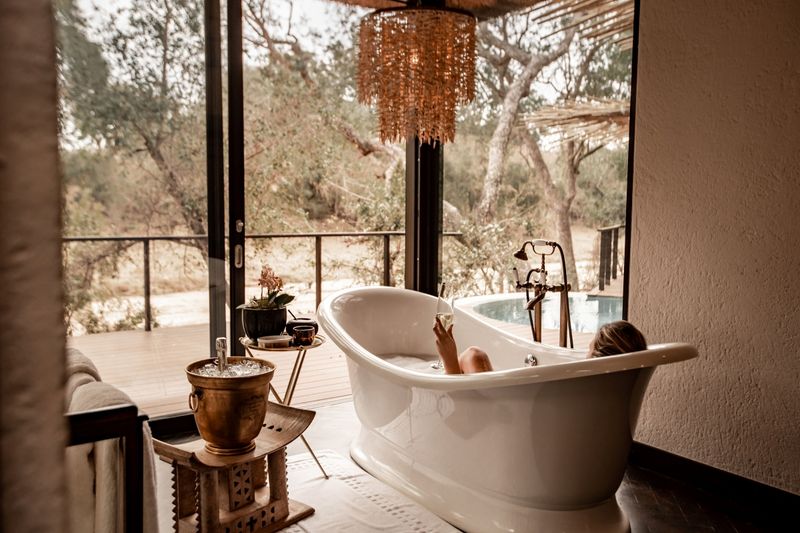 A woman relaxes in a freestanding bath with a glass of bubbly, embracing slow luxury on a return trip to Africa.
