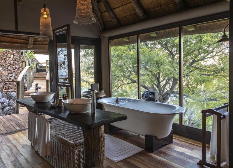 A stand alone bathtub in a luxury safari lodge in Namiba with trees outside the window