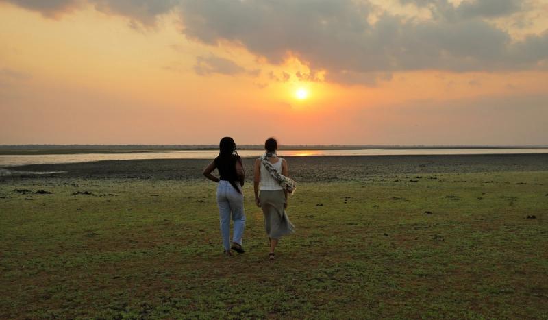 Two travellers walk across an open lakeshore at sunset, offering a quiet glimpse of where to go in 2026.