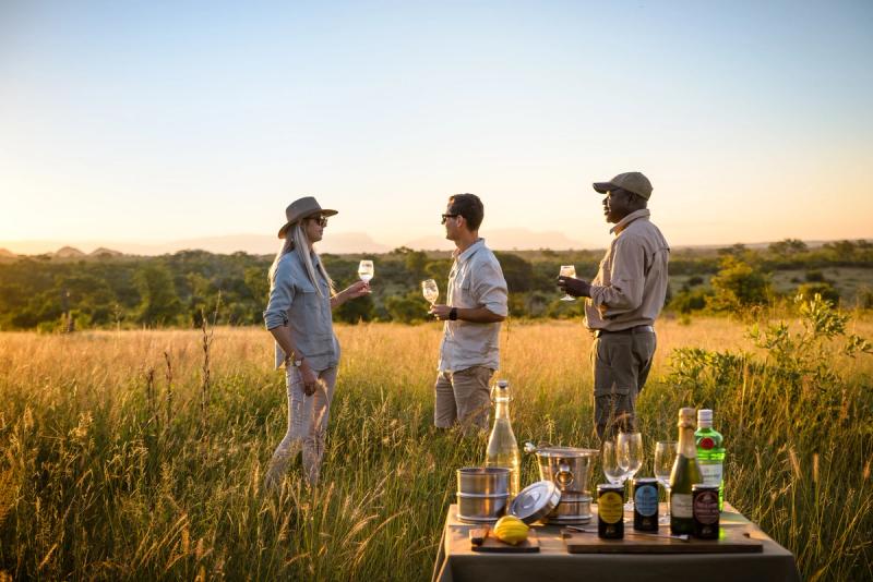 Couple and guide drinking sundowners in the bush at Singita Boulders Lodge, South Africa
