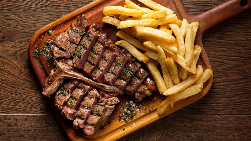 A wooden platter with carved steak and chips