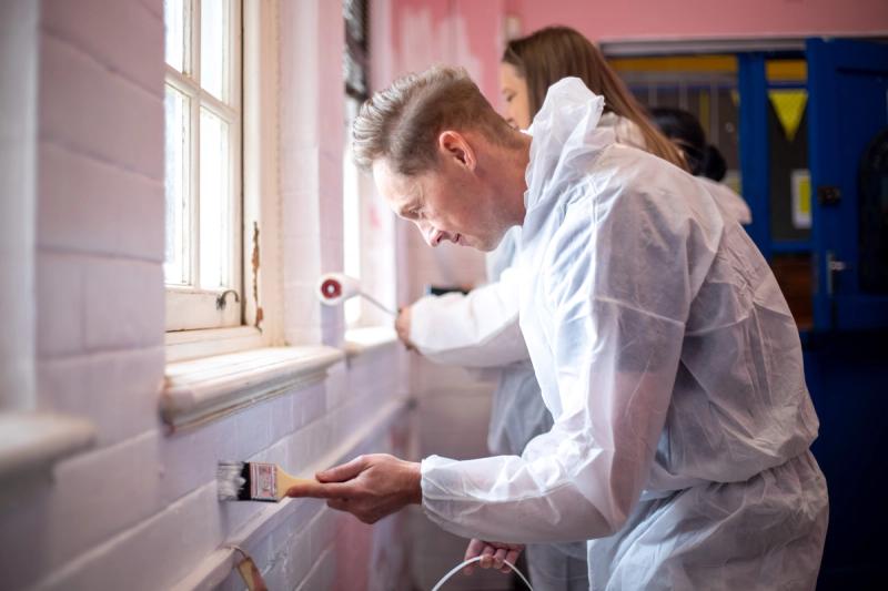 A Rhino Africa volunteer carefully paints a classroom wall near a window during a Mandela Day project