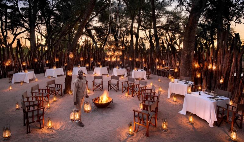 Lanterns glow around a firelit boma where a guide prepares the space for an evening that feels like a living manifesto of connection.