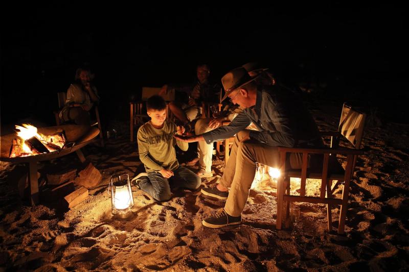 Guests sit around a glowing bonfire at night at Londolozi, sharing conversation in the warm firelight.