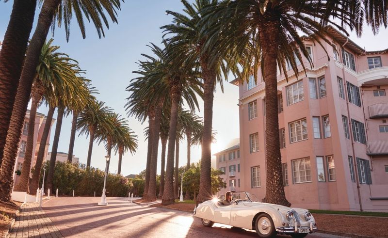 A vintage car parked beneath towering palms outside Mount Nelson, one of the grand luxury hotels in Cape Town