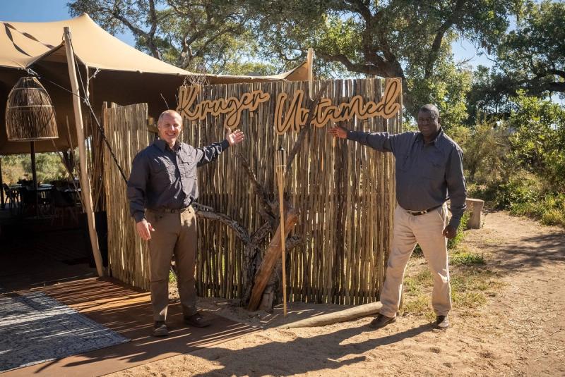 Renias Mhlongo and Alex van den Heever of the Tracker Academy standing at the Kruger Untamed entrance sign.