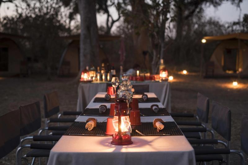 A candlelit dining setup with lanterns and canvas tents forms part of a mobile tented camp in Botswana, ready for guests to gather under the stars.