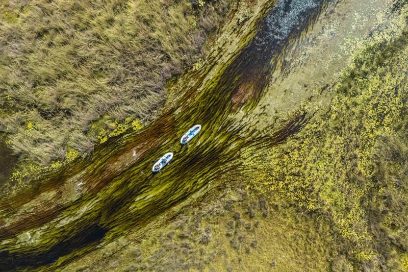 An aerial view shows two small boats drifting along a narrow, reed-lined water channel, exemplifying low-impact destinations for responsible travel.
