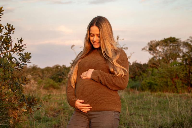 stands in the African bush at sunset, smiling down at her baby bump with her hands gently cradling it during her babymoon safari.