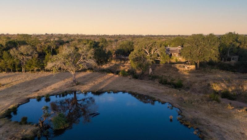 An aerial view shows a secluded safari lodge overlooking a quiet, reflective waterhole surrounded by bushveld, capturing the stillness offered by lodges with the best waterholes.