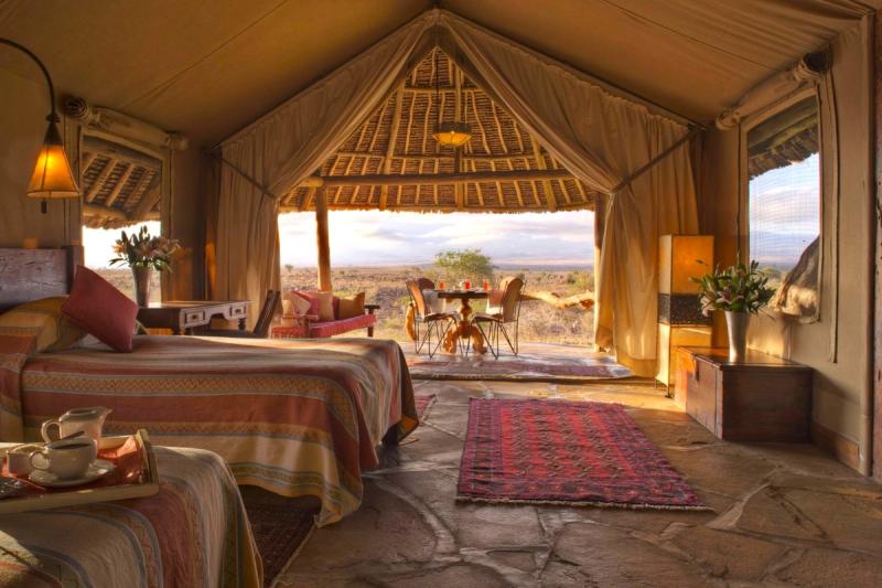 A warmly styled safari tent opens onto a shaded patio with panoramic views