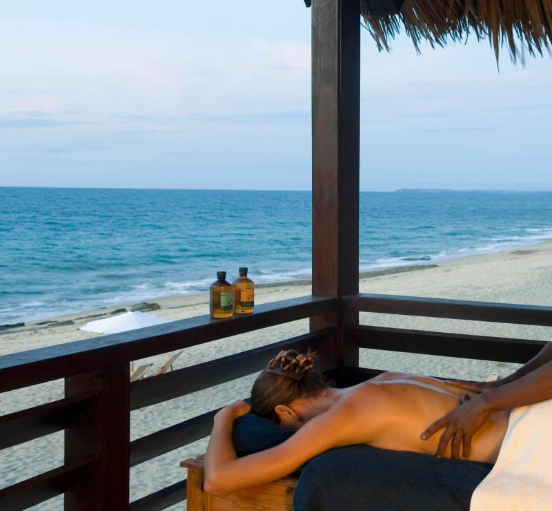 Eine Frau bekommt eine Massage auf einer Terrasse, daneben das Meer und Strand