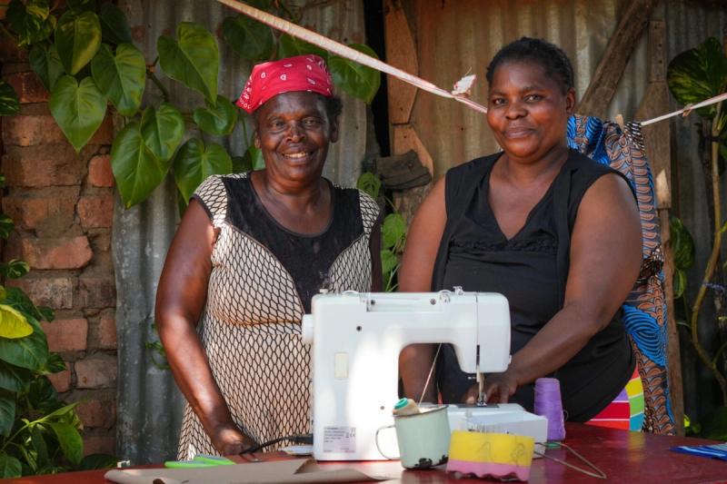 Two women stand behind a sewing machine, crafting unique goods you can purchase on a Zimbabwe safari