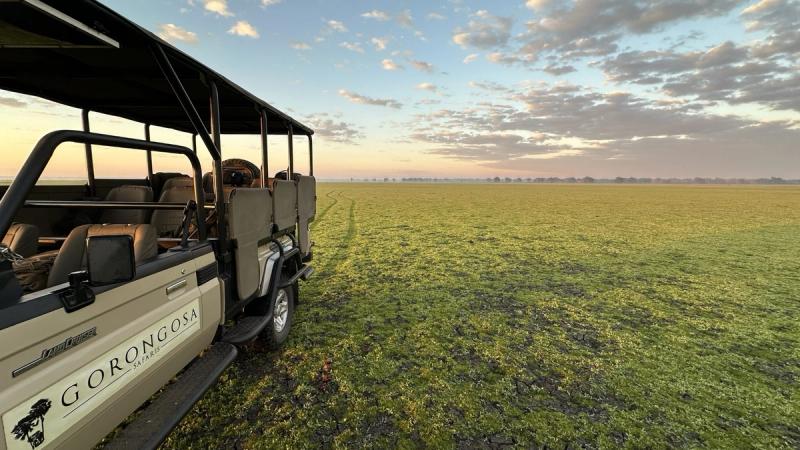 A Gorongosa safari vehicle sits on an open, dew-soaked plain under a soft sunrise sky.